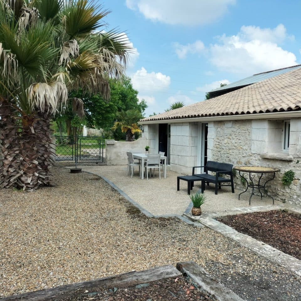 Façade en pierre de La Résidence Zen avec terrasse, mobilier d'extérieur et palmier, Kaza Evasion à Cabariot